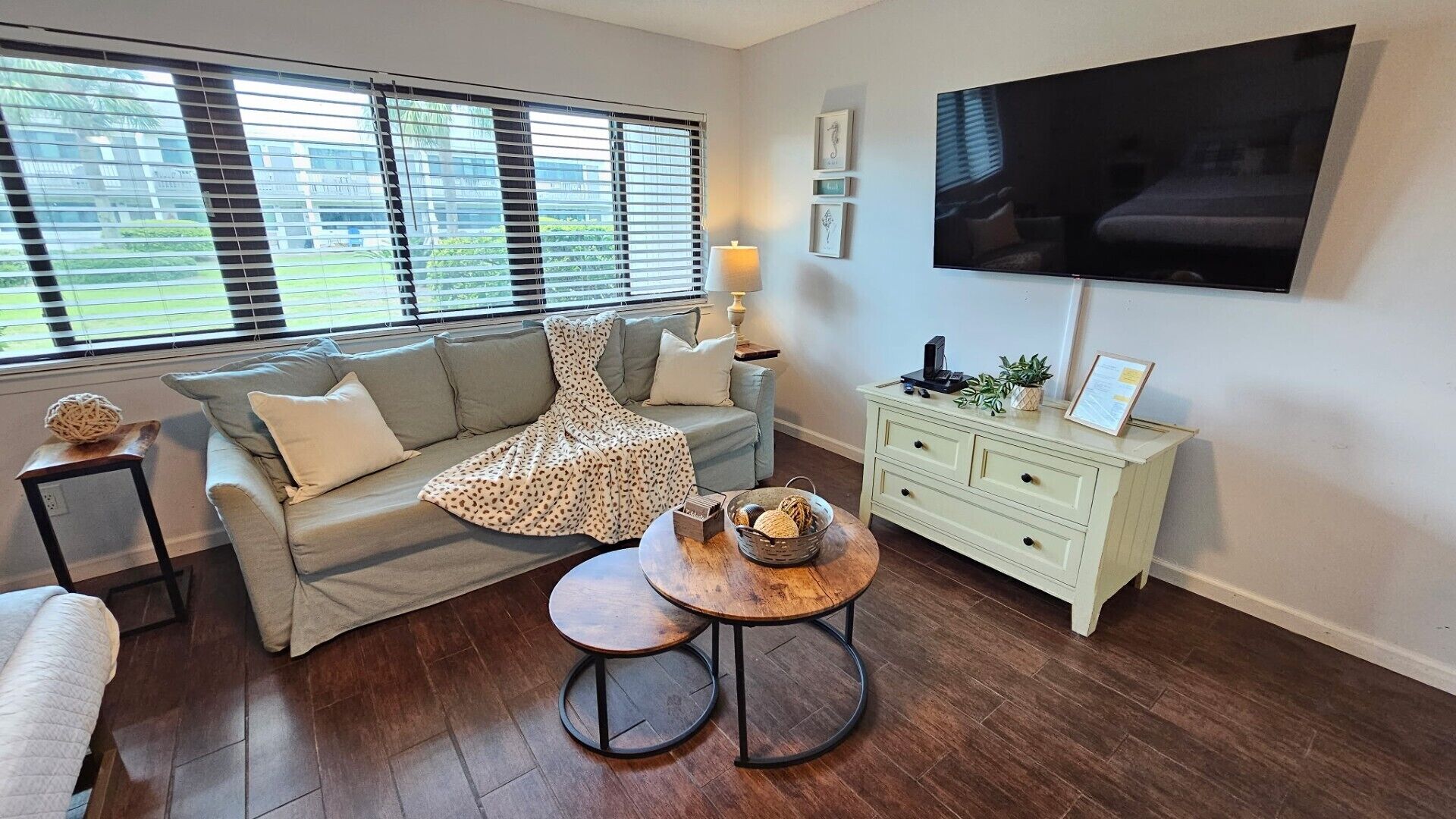 A living room with a sofa, a coffee table, a TV, and a window with blinds.