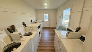 A laundry room with multiple washing machines and dryers, a wooden floor, and a door leading to an outdoor area. - 30-A Getaway near Seaside, FL --Great for Snowbirds, couples, or small families (Santa Rosa Beach)