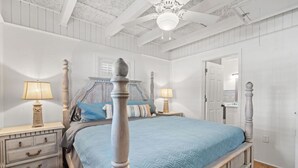 Un dormitorio con una cama con dosel, dos mesitas de noche y un ventilador de techo.