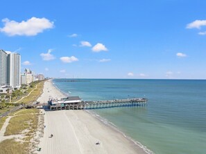Une plage avec une jetée qui s’avance dans l’eau, bordée d’une rangée d’immeubles de grande hauteur.