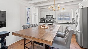 Una cocina moderna con armarios blancos, una mesa de comedor de madera y un refrigerador de acero inoxidable.