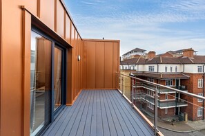 A balcony with a wooden floor and metal railing, overlooking a residential area with brick houses. - Canada Water Suite | 1 bedroom flat | Rotherhithe, London (London)