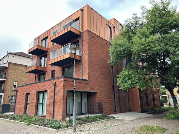 A modern multi-story building with brick facade, balconies, and a paved courtyard.