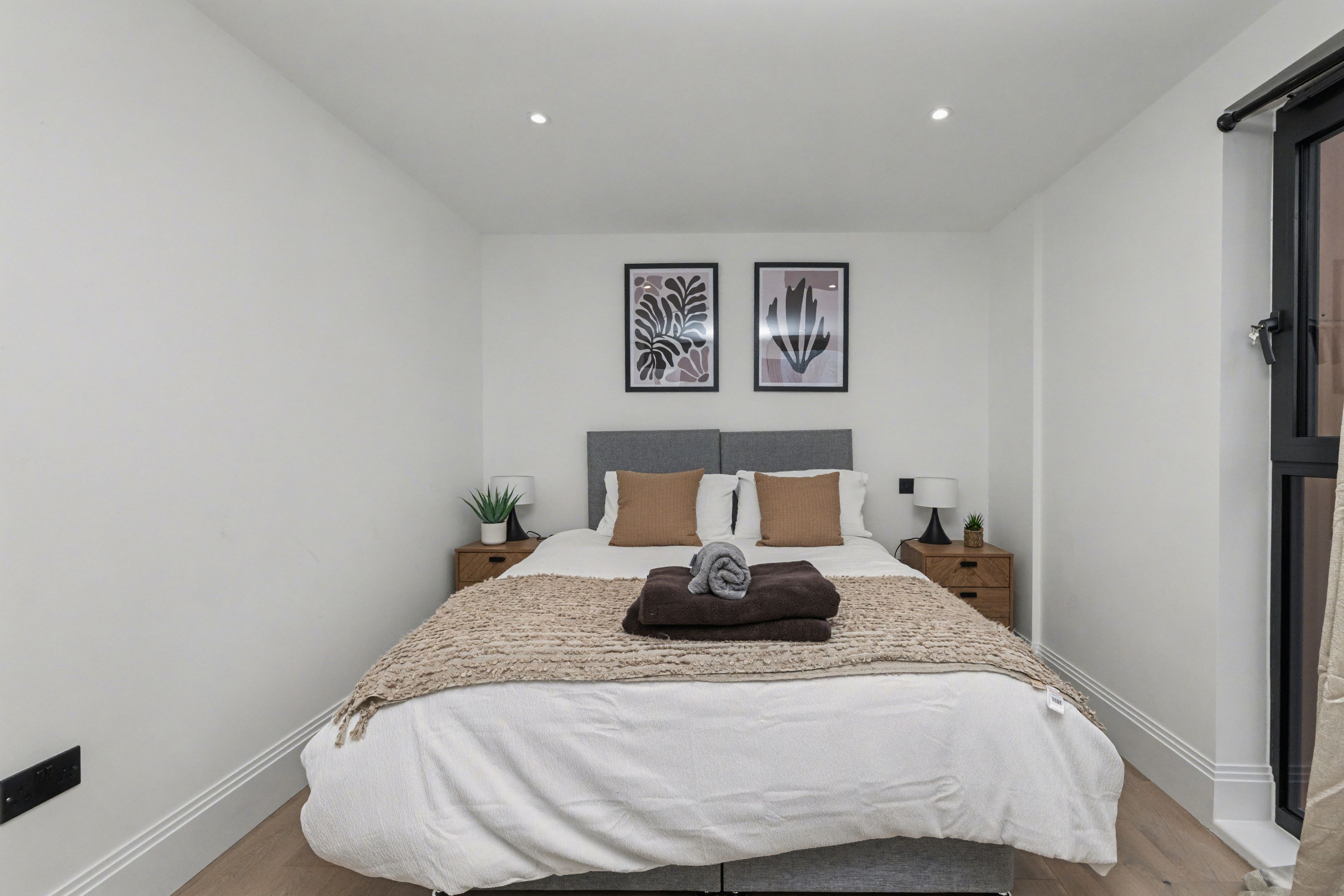A bedroom with a bed, two bedside tables, a nightstand, a headboard, and two wall-mounted artworks.