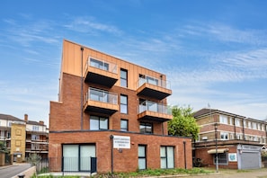 Um edifício de apartamentos moderno com várias andares, varandas, uma placa de identificação visível e um barbeiro ao lado.