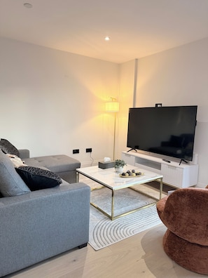 Ein modernes Wohnzimmer mit grauem Sofa, Couchtisch, Flachbildfernseher und Stehlampe.