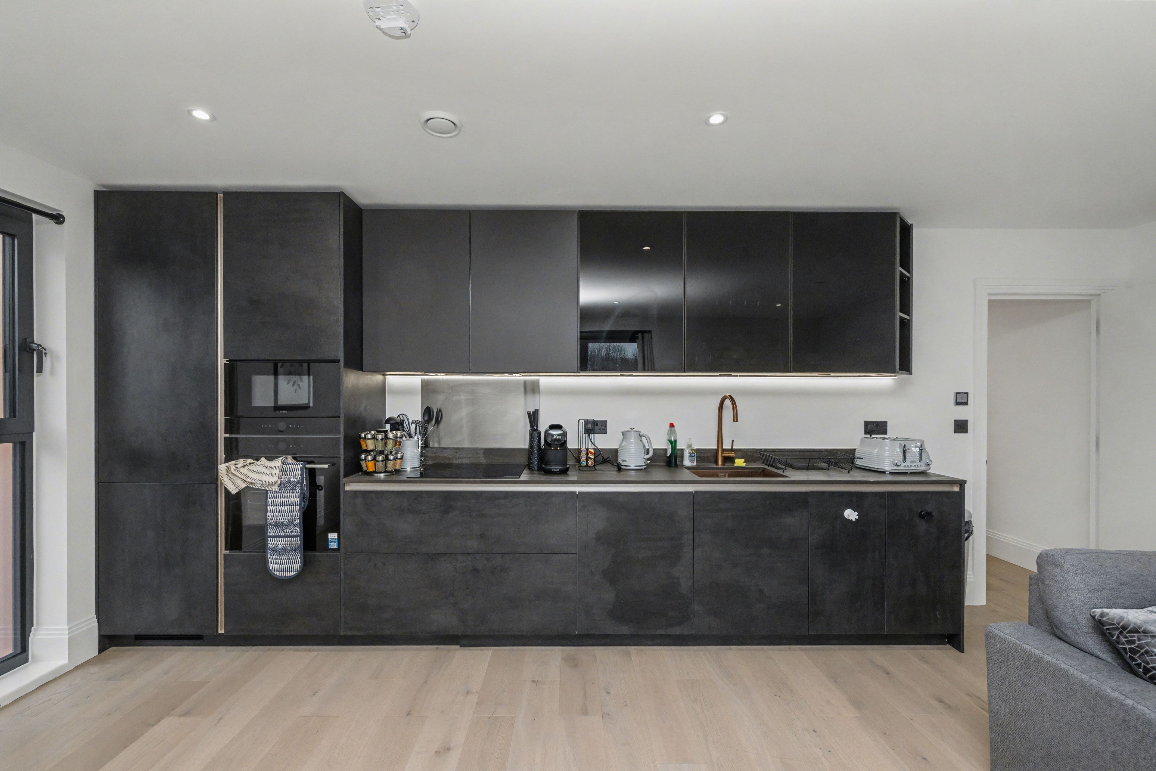 A modern kitchen with dark cabinetry, a central island, and a built-in oven.