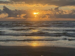Een strand met golven en een ondergaande zon.