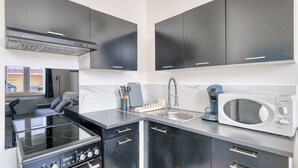 A modern kitchen with black cabinets, a stainless steel stove, a microwave, and a coffee maker. - Charming air-conditioned T2 near Lyon and the metro (Villeurbanne)