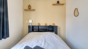 A bedroom with a bed, a bedside table with a lamp, a wall-mounted air conditioner, and decorative items on shelves. - Charming air-conditioned T2 near Lyon and the metro (Villeurbanne)