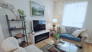 Een woonkamer met een bank, fauteuils, een salontafel, een televisie, een lamp en een boekenkast.