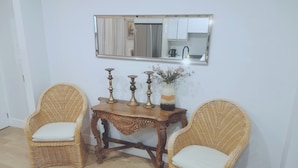 Een kamer met twee rieten stoelen, een houten tafel met decoratieve objecten en een spiegel aan de muur.