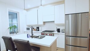 Een moderne keuken met witte kasten, een roestvrijstalen koelkast, een gasfornuis en een barkruk.