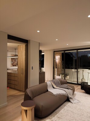 A modern living room with a sofa, a small wooden table, and a large sliding glass door leading to an outdoor area. - Luxury apartment in the heart of Surryhills, close to cafes, bars & so much more (Surry Hills)