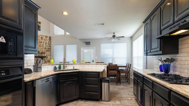 A kitchen with dark cabinetry, a dishwasher, a sink, a stove, and a ceiling fan. - Family Home - Private Pool - Office - Pet Friendly (Fort Worth)