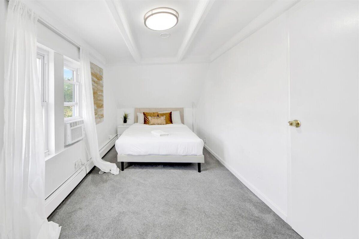 A bedroom with a bed, a nightstand, a window with curtains, and a door.