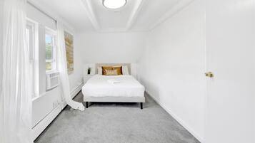 A bedroom with a bed, a nightstand, a window with curtains, and a door.