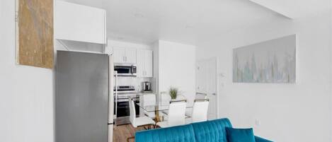 Un salon moderne avec un canapé bleu, un coin cuisine doté de meubles blancs et une table à manger avec des chaises.