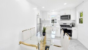 A modern kitchen with white cabinetry, a glass dining table, and stainless steel appliances.