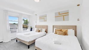 A hotel room with two beds, white bedding, a view through large windows, and abstract wall art.