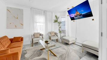 Un salon moderne avec un grand téléviseur à écran plat fixé au mur, une table basse en verre et un canapé.
