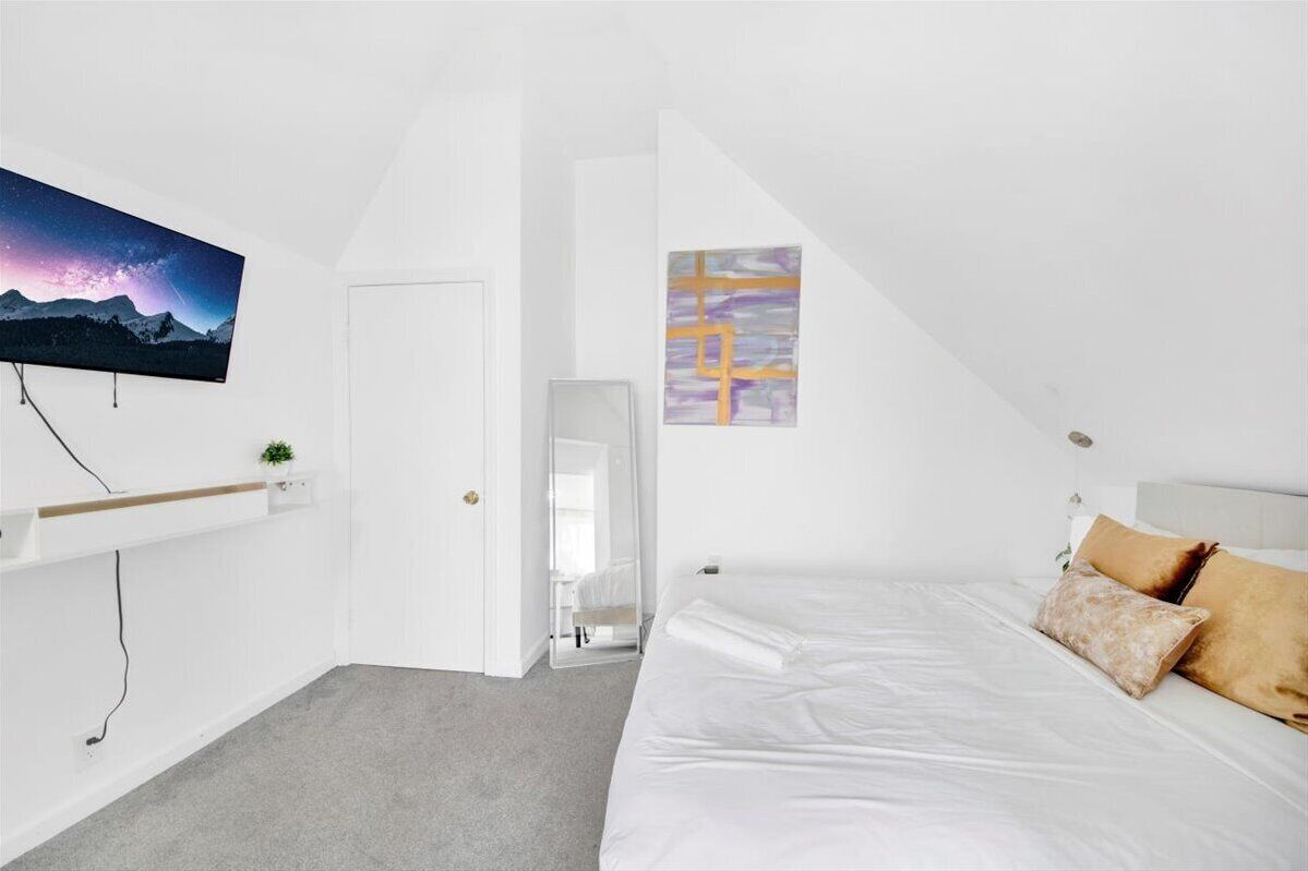 Quarto com cama, TV na parede, um quadro e uma pequena planta.