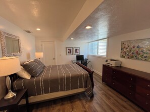 A bedroom with a bed, bedside table, lamp, dresser, desk, chair, and artwork on the wall. - Extended Ski/Work/Visit secluded Cul-da-sac cutie (Salt Lake City)