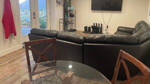 A living room with a black leather sofa, a glass coffee table, and a TV mounted on the wall. - Extended Ski/Work/Visit secluded Cul-da-sac cutie (Salt Lake City)