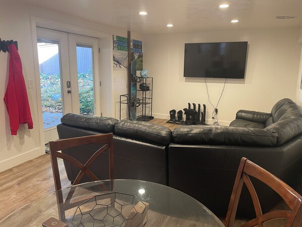 A living room with a black leather sofa, a glass coffee table, and a TV mounted on the wall. - Extended Ski/Work/Visit secluded Cul-da-sac cutie (Salt Lake City)