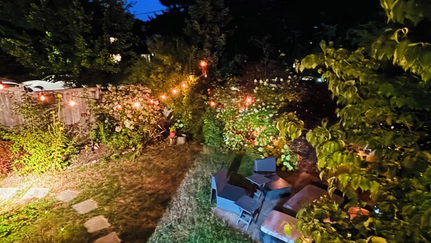 Un jardín con un sendero de piedra, plantas en macetas y luces colgantes.