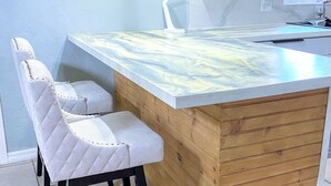 Cocina con una isla de madera, dos taburetes de bar y una encimera blanca.