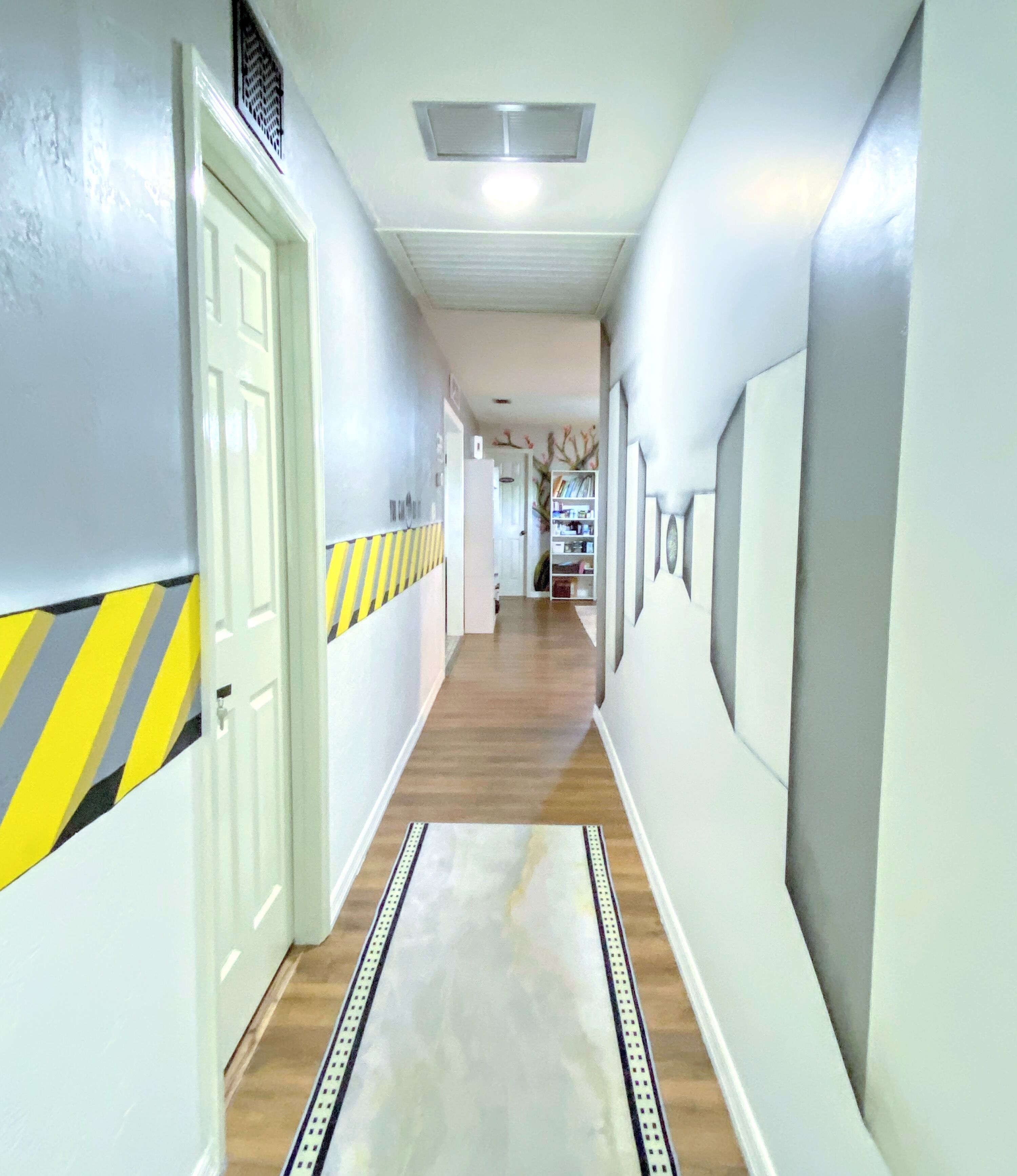 A hallway with a wooden floor, white walls, and a striped safety line on the left.