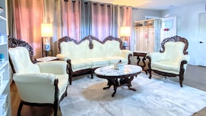 Una sala de estar con un sofá blanco, dos sillones, una mesa redonda de centro y una araña.