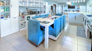 Una cocina moderna con armarios blancos, una isla central con asientos acolchados azules y una mesa de comedor.