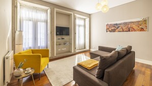 Un salon moderne avec un canapé, un fauteuil jaune, un téléviseur à écran plat et un tableau accroché au mur.