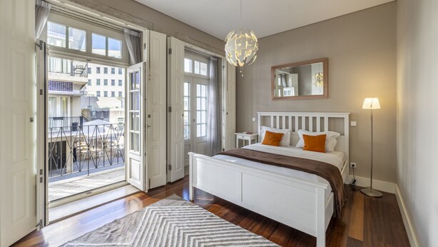 Une chambre à coucher avec un lit, une table de chevet, une lampe, un miroir et une vue sur l’extérieur.