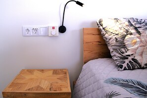 Et soveværelse med et trænatbord, en seng med pude med blomstermønster, en stikkontakt og en sort lampe.