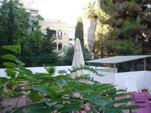 A rooftop terrace with a white umbrella, a white chair, and a pink towel. - Hostel Albergue Studio (Barcelona)