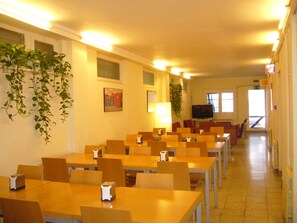 A dining area with multiple tables and chairs, a television, and hanging plants. - Hostel Albergue Studio (Barcelona)