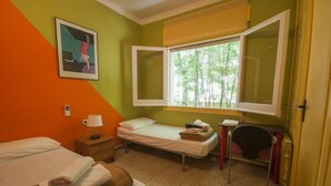 A room with two beds, a desk, a chair, and a window with a view of trees. - Hostel Albergue Studio (Barcelona)