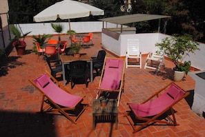An outdoor patio with brick flooring, wooden and plastic chairs, a table, and umbrellas providing shade. - Hostel Albergue Studio (Barcelona)