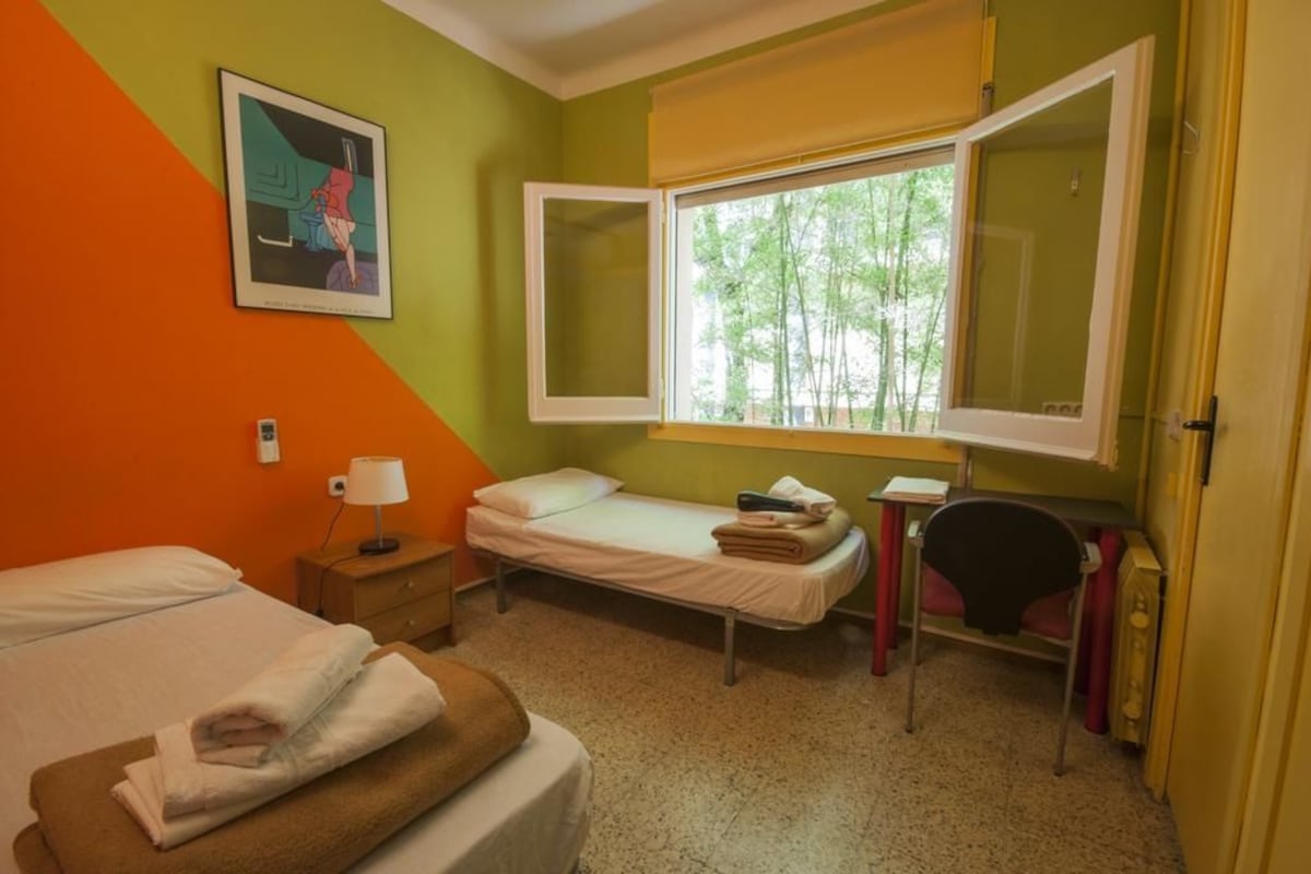 A room with two beds, a desk, a chair, and a window with a view of trees.