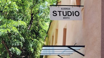 A sign for 'Albergue Studio Hostel' with a view of a tree and a building facade.