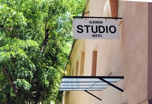 Une enseigne indiquant « Albergue Studio Hostel », avec en arrière-plan un arbre et la façade d’un immeuble.