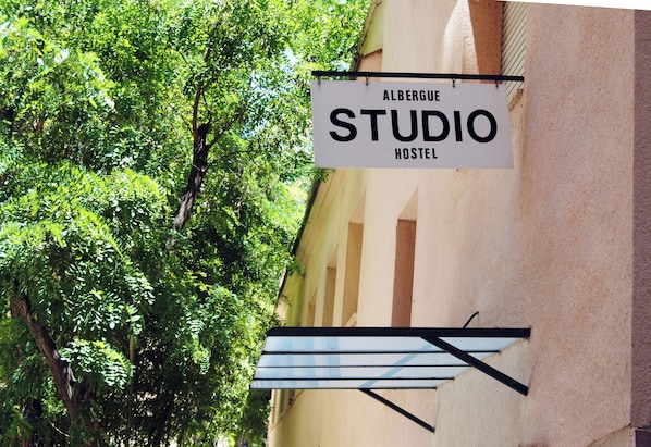 A sign for 'Albergue Studio Hostel' with a view of a tree and a building facade. - Hostel Albergue Studio (Barcelona)