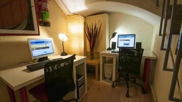 A small office with two desks, each with a computer and a lamp. There is a fire extinguisher on the wall and a plant in the corner.