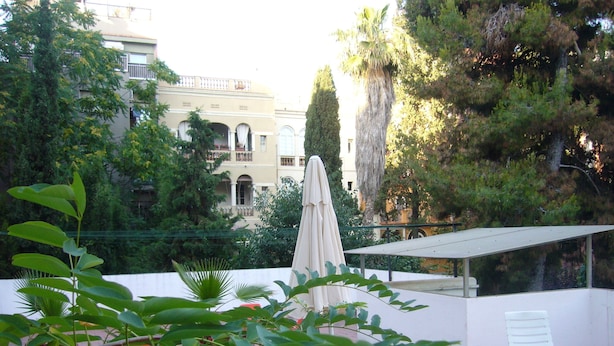 A rooftop terrace with a white umbrella, a white chair, and a pink towel. - Hostel Albergue Studio (Barcelona)