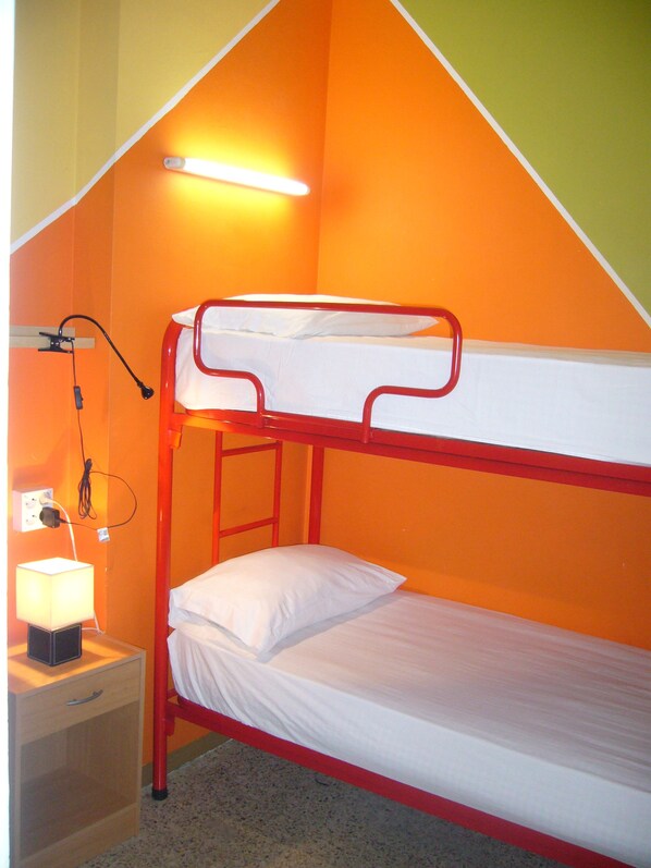 A bunk bed with a single bed below, a nightstand with a lamp, and a wall socket. - Hostel Albergue Studio (Barcelona)