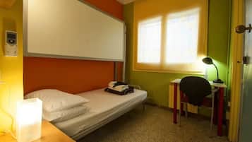 A single-bed room with a desk, chair, and a window providing natural light.