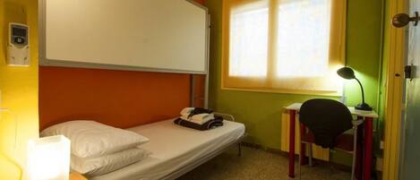 A single-bed room with a desk, chair, and a window providing natural light.
